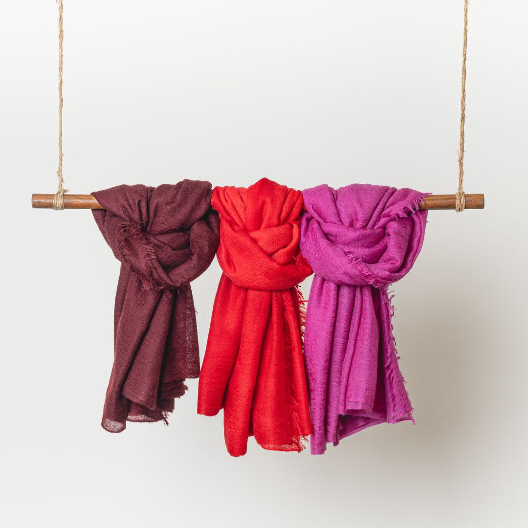 100% cashmere felted shawls hanging left to right in cabernet, red, and pink
