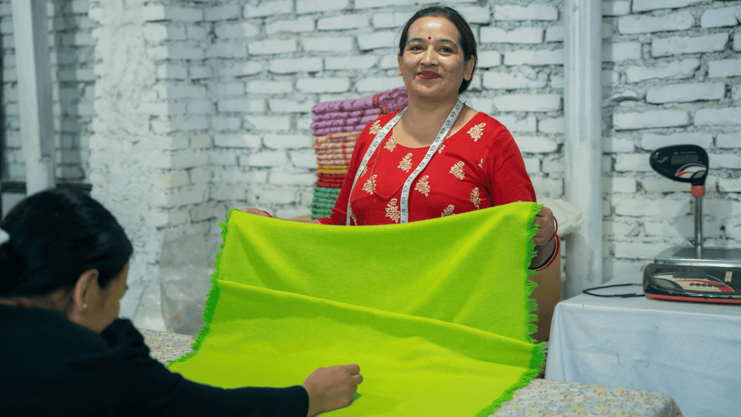 A Nepalese Artisan holding a near-finished green shawl with measuring tape wrapped around her neck