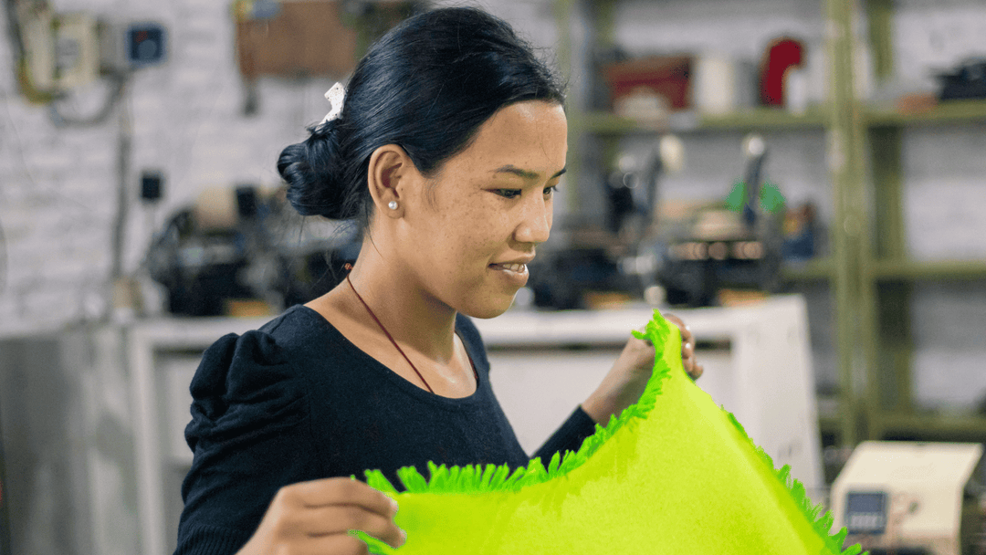 A young Nepali woman is folding a bright green scarf before it is packaged for sale