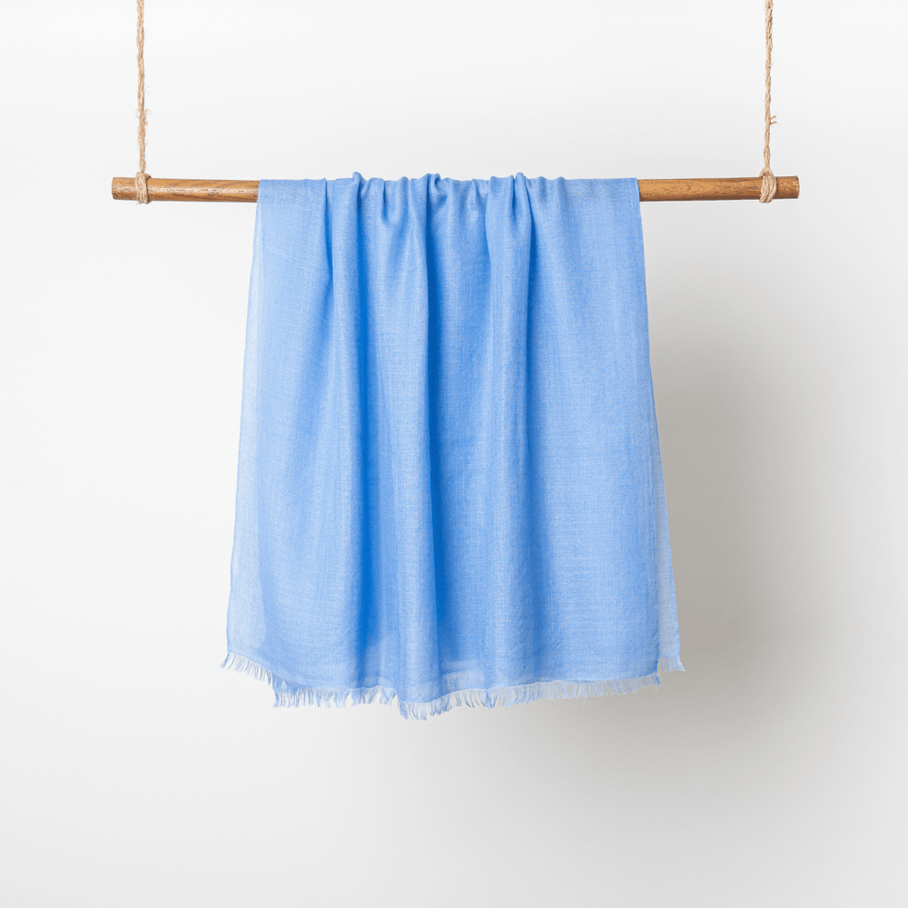 Blue Tint 100% Cashmere Ring Scarf displaying raw edges hanging on a wooden dowel rod wrapped in twine on both ends#color_blue-tint