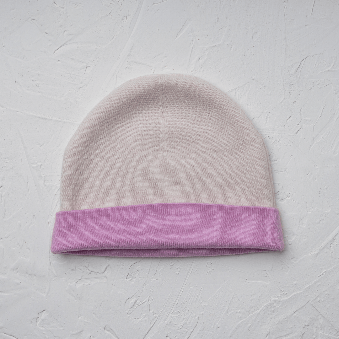 Reversible 100% Cashmere Beanie in Tender Touch(Pink) and Blanc de Blanc(White) laid flat on a white drywall#color_tender-touch-and-blanc-de-blanc