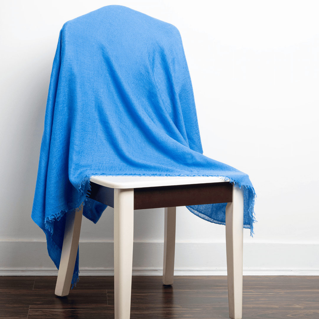 Blue 100% Cashmere Felted Shawl draped over a white-painted wooden chair with white wall background on dark brown wood floor#color_blue