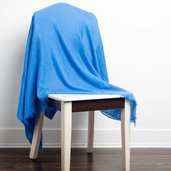 Blue 100% Cashmere Felted Shawl draped over a white-painted wooden chair with white wall background on dark brown wood floor#color_blue