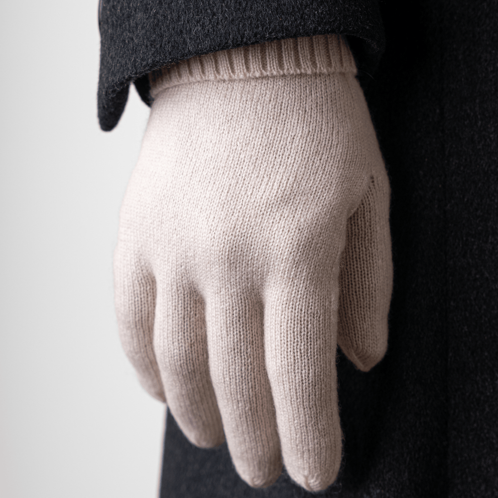 Sea Salt 100% Cashmere Gloves worn on the right hand held down by the side of a body wearing a dark grey trench coat#color_sea-salt