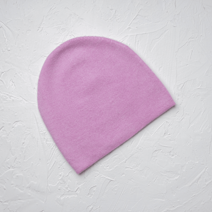 Pink side of Reversible 100% Cashmere Beanie in Tender Touch(Pink) and Blanc de Blanc(White) laid flat on white drywall#color_tender-touch-and-blanc-de-blanc